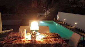 Area ristoro a bordo piscina con tavolo apparecchiato per due, piscina e montagne sullo sfondo.