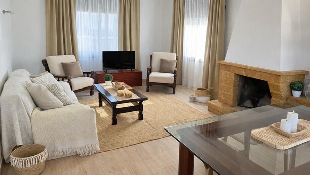 Ein Wohnzimmer mit einer Sofagarnitur, einem Couchtisch, einem Fernseher, einem Kamin und Vorhängen.