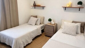 Ein Hotelzimmer mit zwei Betten, einem kleinen Nachttisch mit Lampe sowie Wandregalen mit Dekoration.
