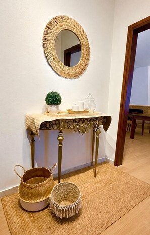Ein Zimmer mit einem runden Spiegel, einem kleinen Tisch mit Dekoration und zwei gewebten Körben auf einem Teppich.