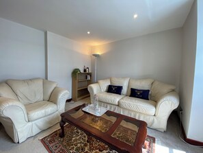 Ein Wohnzimmer mit zwei weißen Ledersofas, einem Holztisch und einem Bücherregal.