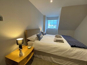 Ein Schlafzimmer mit Bett, Nachttisch, Lampe und einem Fenster mit Blick.