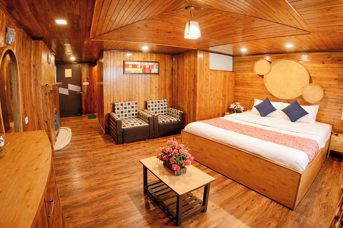 Een kamer met houten inrichting, een bed, twee stoelen, een klein tafeltje met bloemen en een houten plafond.