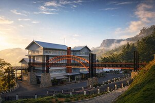 Um hotel grande com uma imponente ponte em arco, pilares de pedra e montanhas ao fundo.