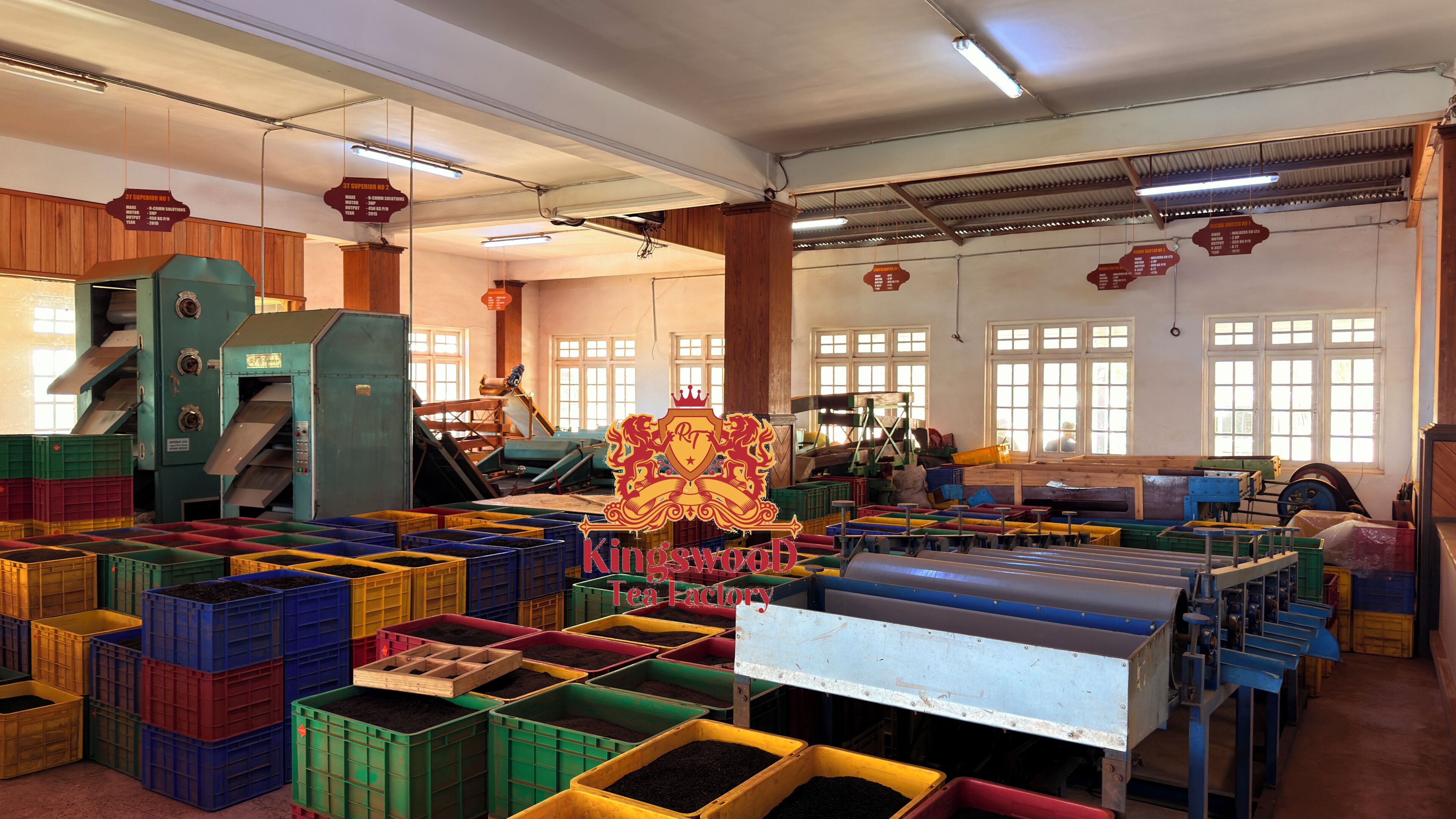 A spacious industrial facility with large machinery, storage bins, and a prominent sign reading 'Kingswood Tea Factory.'