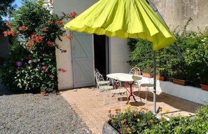 An outdoor patio with a table and chairs, a yellow umbrella, and potted plants.