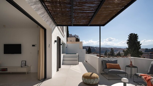 Eine moderne Dachterrasse mit flachem Dach, einer Couch, einem runden Hocker, einem kleinen Tisch und einem an der Wand montierten Fernseher.