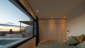 Ein Schlafzimmer mit großem Fenster, einem Bett mit Kissen, einem Nachttisch und einem Kleiderschrank.