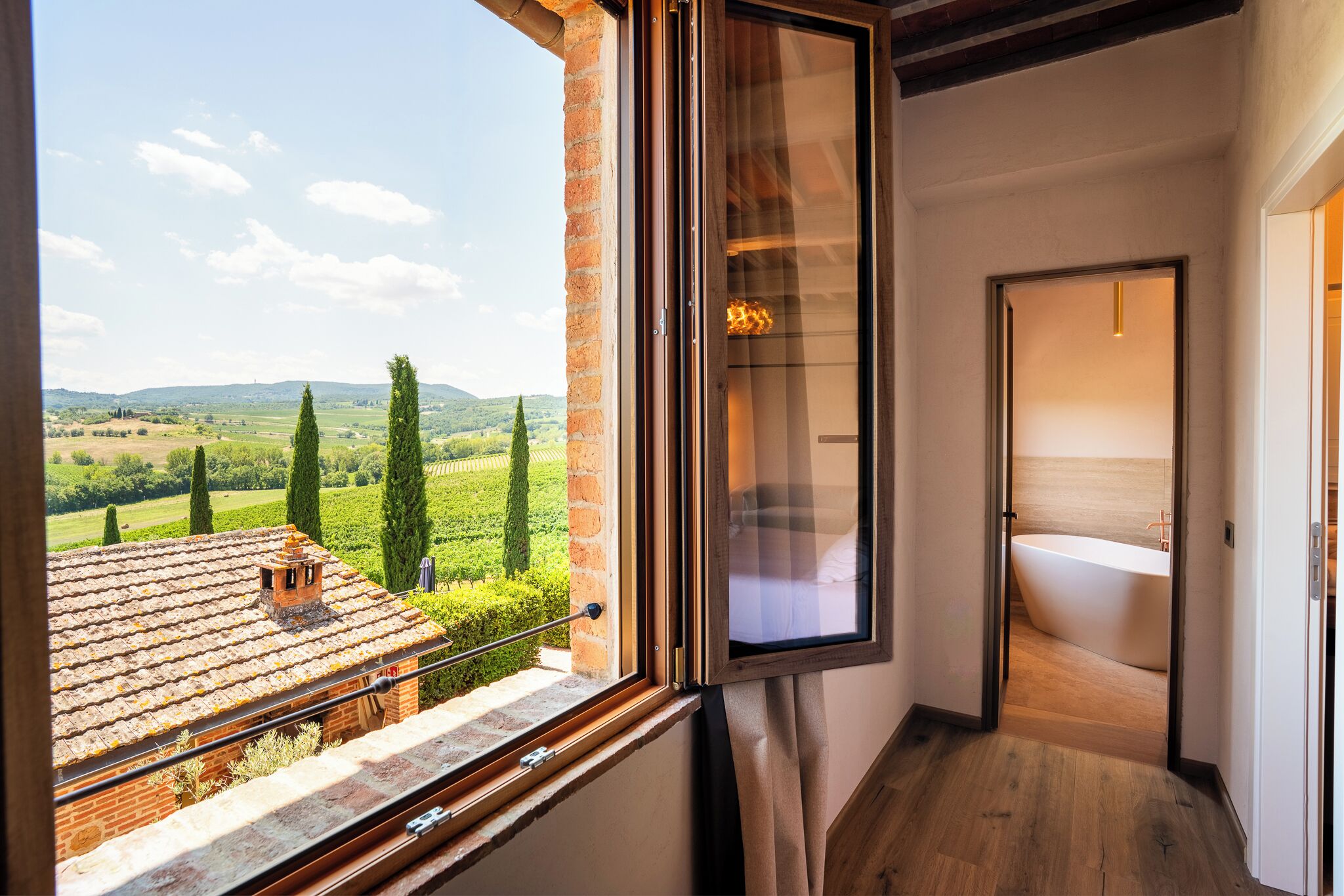 Una habitación con un amplio ventanal con vistas a un viñedo, piso de madera y baño con bañera.
