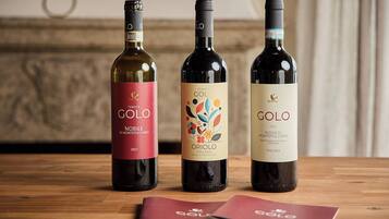Tre flasker Tenuta Golo vin på et træbord med en rød brochure ved siden af.