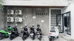 A parking area with multiple motorcycles, air conditioning units, and a building with 'ESCOTEL' signage. - Escotel Vanili Canggu (Tibubeneng)