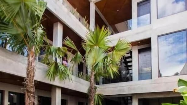 A modern multi-story building with a central pool, surrounded by palm trees. - Escotel Vanili Canggu (Tibubeneng)