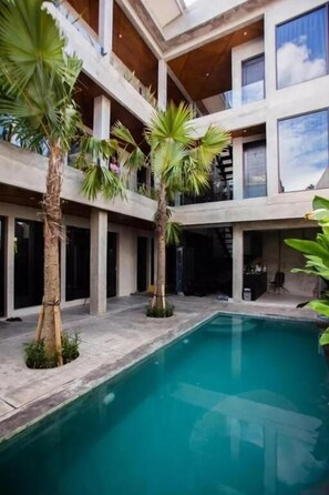 Un moderno edificio de varios pisos con piscina central, rodeado de palmeras.