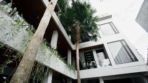 A modern building with a central atrium, a palm tree, and a balcony with plants. - Escotel Vanili Canggu (Tibubeneng)