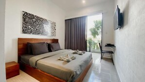 A hotel room with a bed, a TV mounted on the wall, a window with curtains, and a small table. - Escotel Vanili Canggu (Tibubeneng)