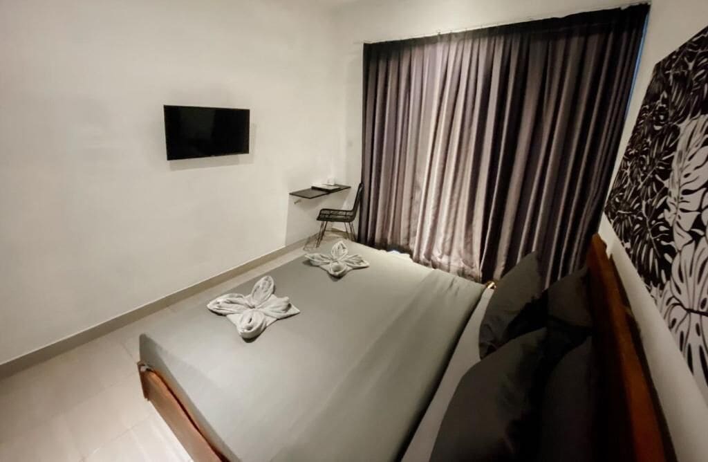 Ett hotellrum med en säng, en tv som är monterad på väggen, ett litet bord och en stol.