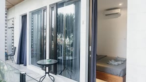 A room with a bed, a small table, and a sliding glass door leading to an outdoor area. - Escotel Vanili Canggu (Tibubeneng)