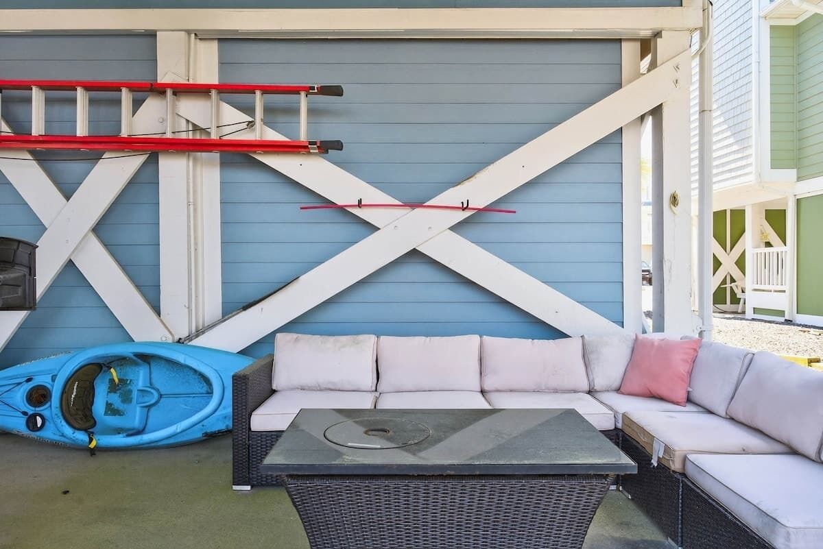 A blue wall with white X-shaped beams, a white sofa with cushions, a blue kayak, and a red ladder.
