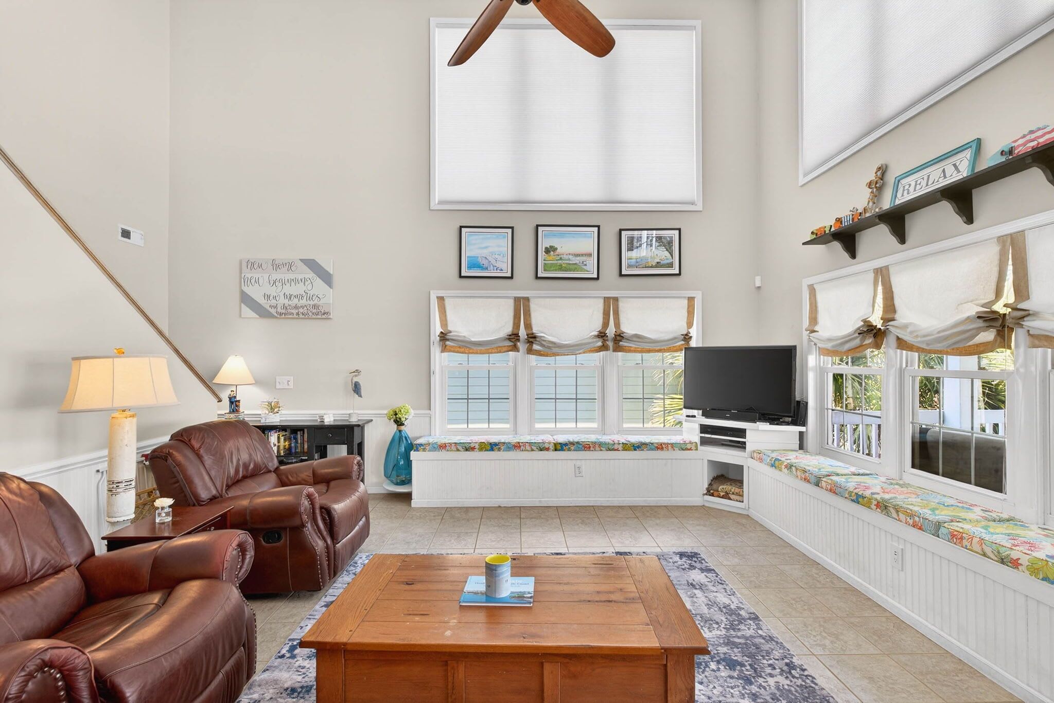 A living room with a sofa, coffee table, and a TV. There are pictures on the wall and a window with curtains.