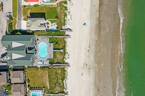 An aerial view of a coastal hotel with a swimming pool, beach access, and a parking area. - Chonky Waves by Brunswick VR: 4BR Condo w/ Ocean Views & Resort Amenities (Ocean Isle Beach)