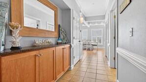 A hallway with a wooden cabinet, a large mirror, and a welcome sign. - Chonky Waves by Brunswick VR: 4BR Condo w/ Ocean Views & Resort Amenities (Ocean Isle Beach)