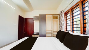 A hotel room with a bed, a wardrobe, a desk with a lamp, and a window with curtains. - Super Townhouse Kalady (Aluva)