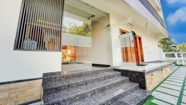 A modern building with a staircase leading to a covered entrance, a glass door, and a small outdoor area with a pathway. - Super Townhouse Kalady (Aluva)