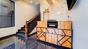 A reception desk labeled 'TOWNHOUSE' with a company-serviced sign, a staircase with wooden railings, and a marble-patterned wall. - Super Townhouse Kalady (Aluva)