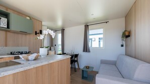 A modern kitchen with a central island, a dining area with a table and chairs, and a living area with a sofa. - Caravan Bredene by the sea (Bredene)