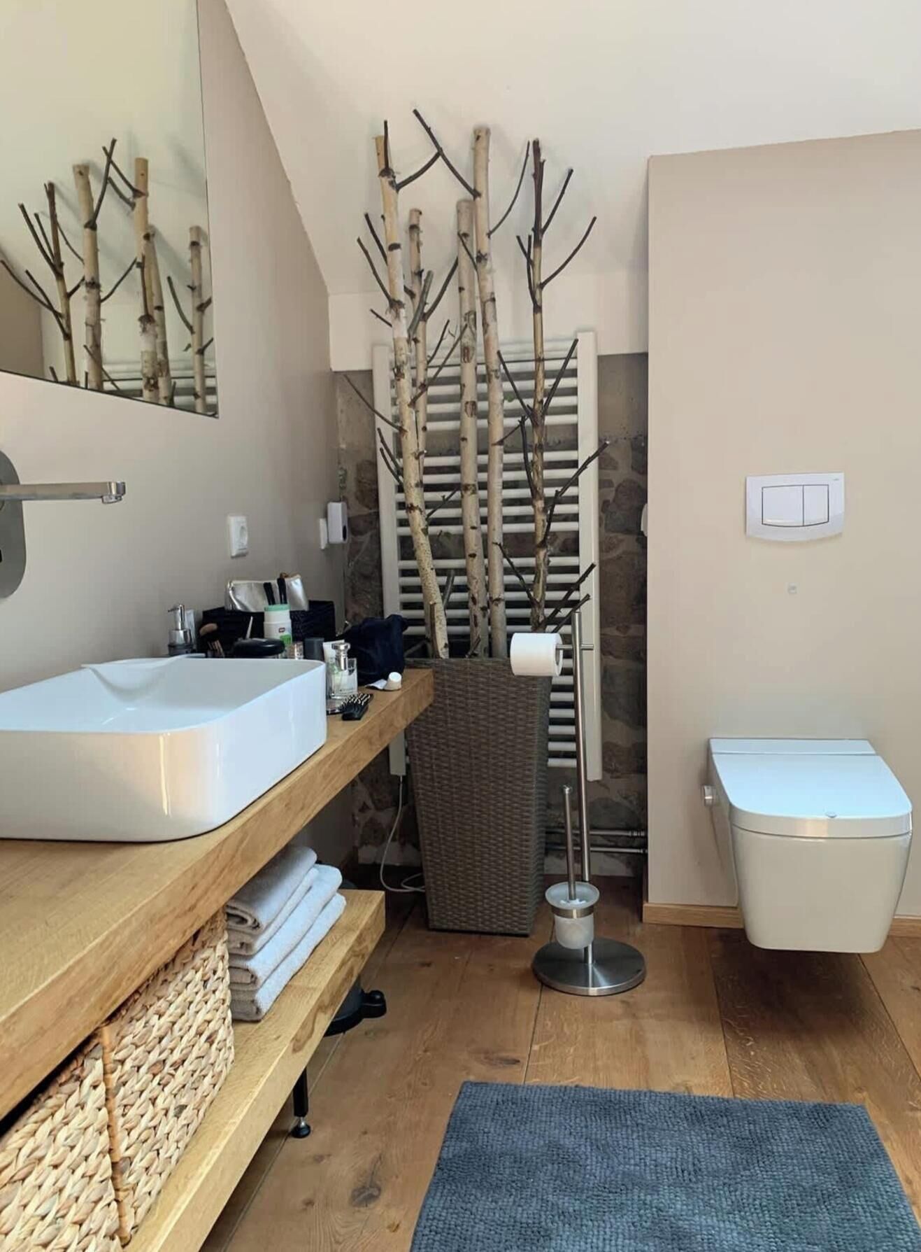 Une salle de bain avec un meuble-lavabo en bois, un lavabo blanc, un miroir, un porte-serviettes, un panier en osier, des toilettes et un radiateur fixé au mur.