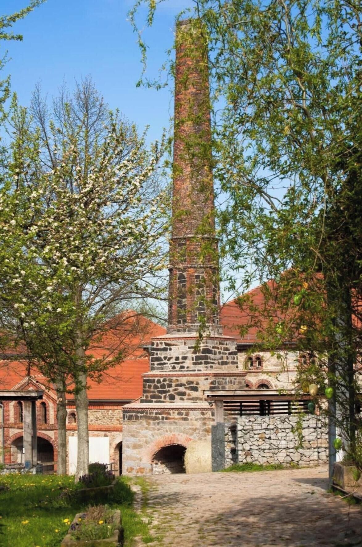 A historic building with a tall chimney, stone arches, and a cobblestone path.