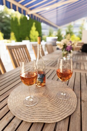 Zwei Gläser Roséwein auf einem Holztisch mit Untersetzer aus Flechtwerk, eine Flasche Roséwein und im Hintergrund eine Vase mit Blumen.