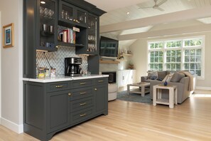 A modern kitchen with dark cabinetry, a coffee machine, and a dining area with a sofa and coffee table. - No crowds after Labor Day Week on Cape Cod  at Old Silver Beach (Falmouth)