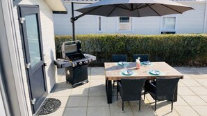 Eine Terrassenanlage im Freien mit Grill, Esstisch, Stühlen und einem großen Sonnenschirm.