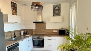 Una cocina moderna con armarios blancos, horno integrado, microondas, tostadora y lámpara colgante.