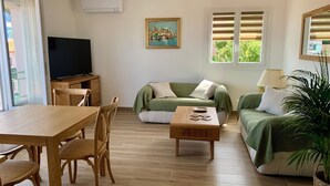 Una sala de estar con una mesa de madera, sillas, un sofá, un televisor y un cuadro en la pared.