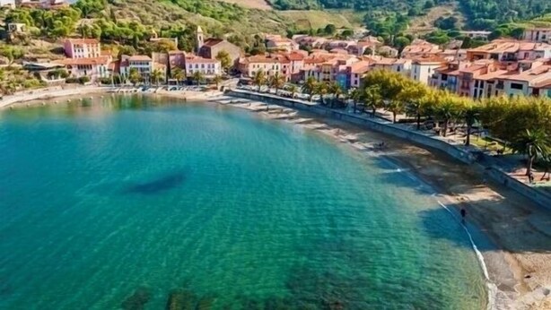 Un pueblo costero con aguas azules cristalinas, una playa y edificios de techos rojos.