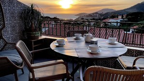 Una terraza con una mesa preparada para el té, sillas y vistas al mar al atardecer.
