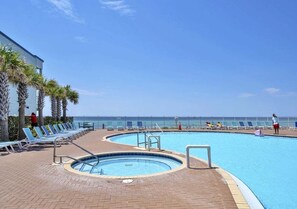 A pool area with lounge chairs and a view of the ocean. - Coastal Calm 1411-Gulf Views-Sleeps 8 (Panama City Beach)
