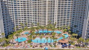 Un hotel moderno de gran altura con varias piscinas rodeado de palmeras y tumbonas.