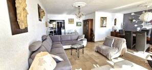 Ein Wohnzimmer mit grauem Sofa, einem runden Couchtisch und einem Essbereich mit Tisch und Stühlen.