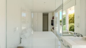 Un baño moderno con cabina de ducha de vidrio, un lavabo blanco y vistas a zonas verdes.