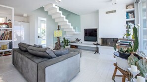Una sala moderna con un sofá gris, una escalera, un televisor de pantalla plana y una chimenea.