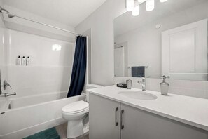 Et moderne badeværelse med badekar, toilet og vaskebord med spejl.