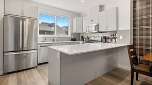A modern kitchen with stainless steel appliances, a large island, and a view of the outdoors. - Luxurious 4BR Home | Near Banff | YYC | Garage (Calgary)