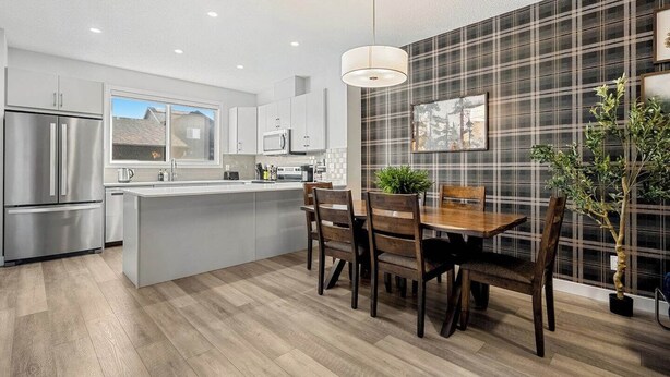 A modern kitchen with a central island, stainless steel appliances, and a dining area with wooden chairs. - Luxurious 4BR Home | Near Banff | YYC | Garage (Calgary)