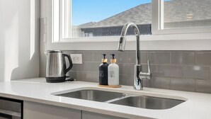 A kitchen with a double sink, a kettle, and two soap dispensers on the counter. - Luxurious 4BR Home | Near Banff | YYC | Garage (Calgary)