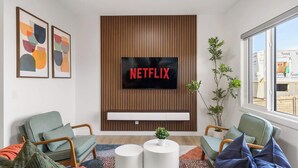 Moderni olohuone, jossa on Netflix-palveluun yhdistetty televisio, kaksi nojatuolia, sohvapöytä ja suuri ikkuna.