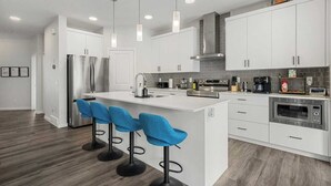 Una cocina moderna con armarios blancos, electrodomésticos de acero inoxidable, una isla central con taburetes azules e iluminación colgante.