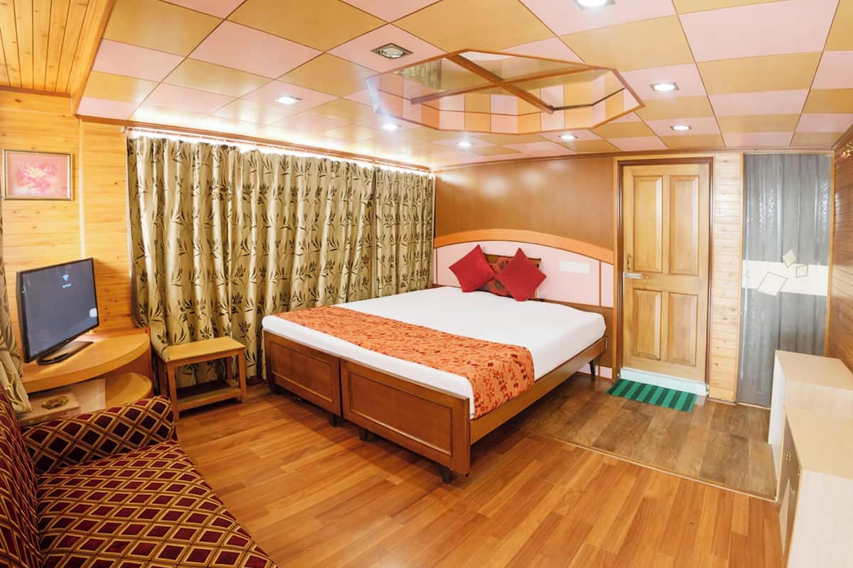 Une chambre d’hôtel avec un lit en bois, un téléviseur posé sur un meuble en bois, une petite table de chevet, un canapé et une armoire en bois.